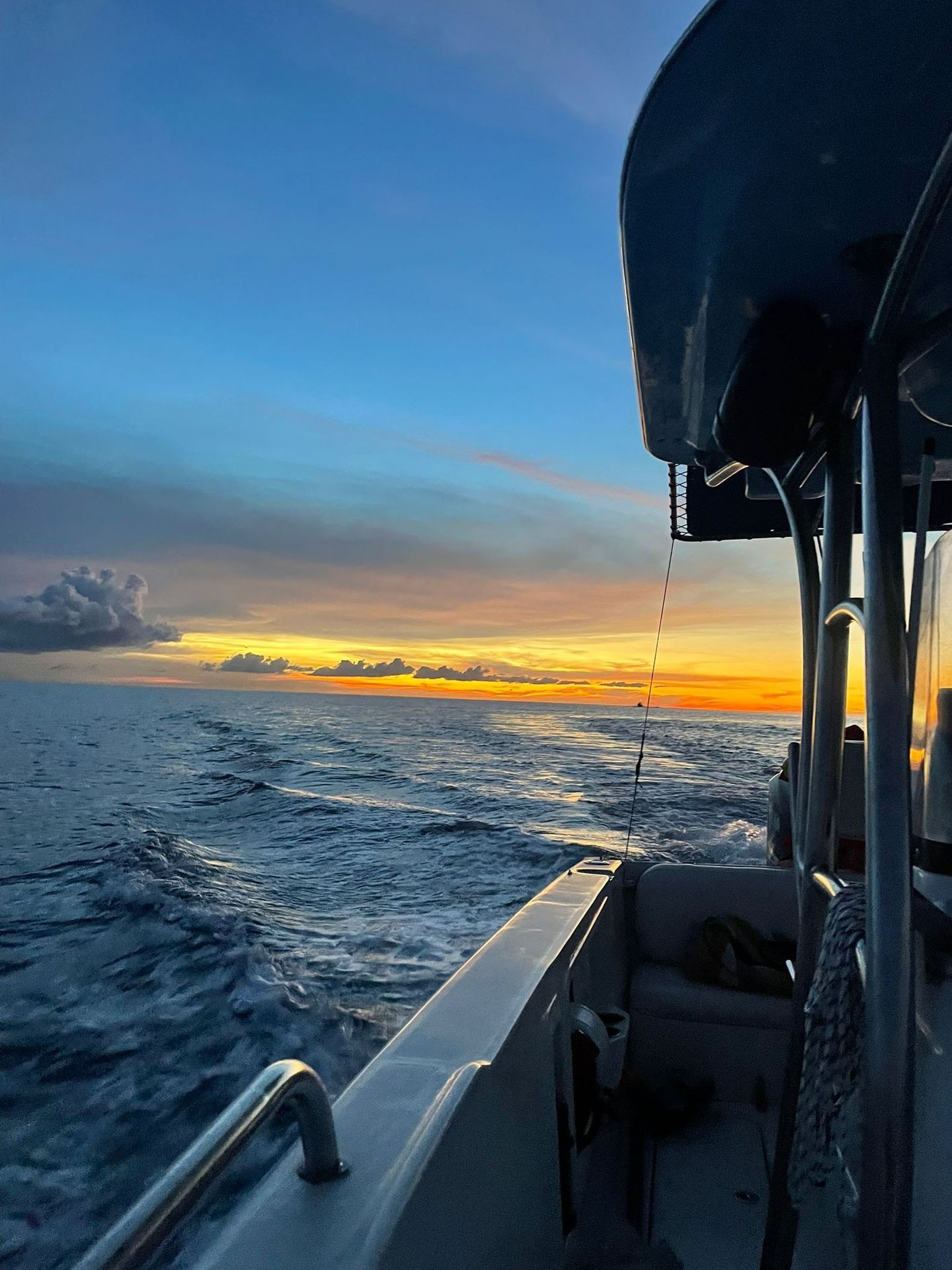 Boat sailing on the ocean during colorful sunset with clouds and waves visible.